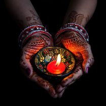 42855543 - woman hands with henna holding lit candle isolated on black background with clipping path